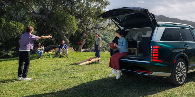 A green 2026 Hyundai Palisade three-row SUV parked outdoors with its rear hatch open during a family gathering.